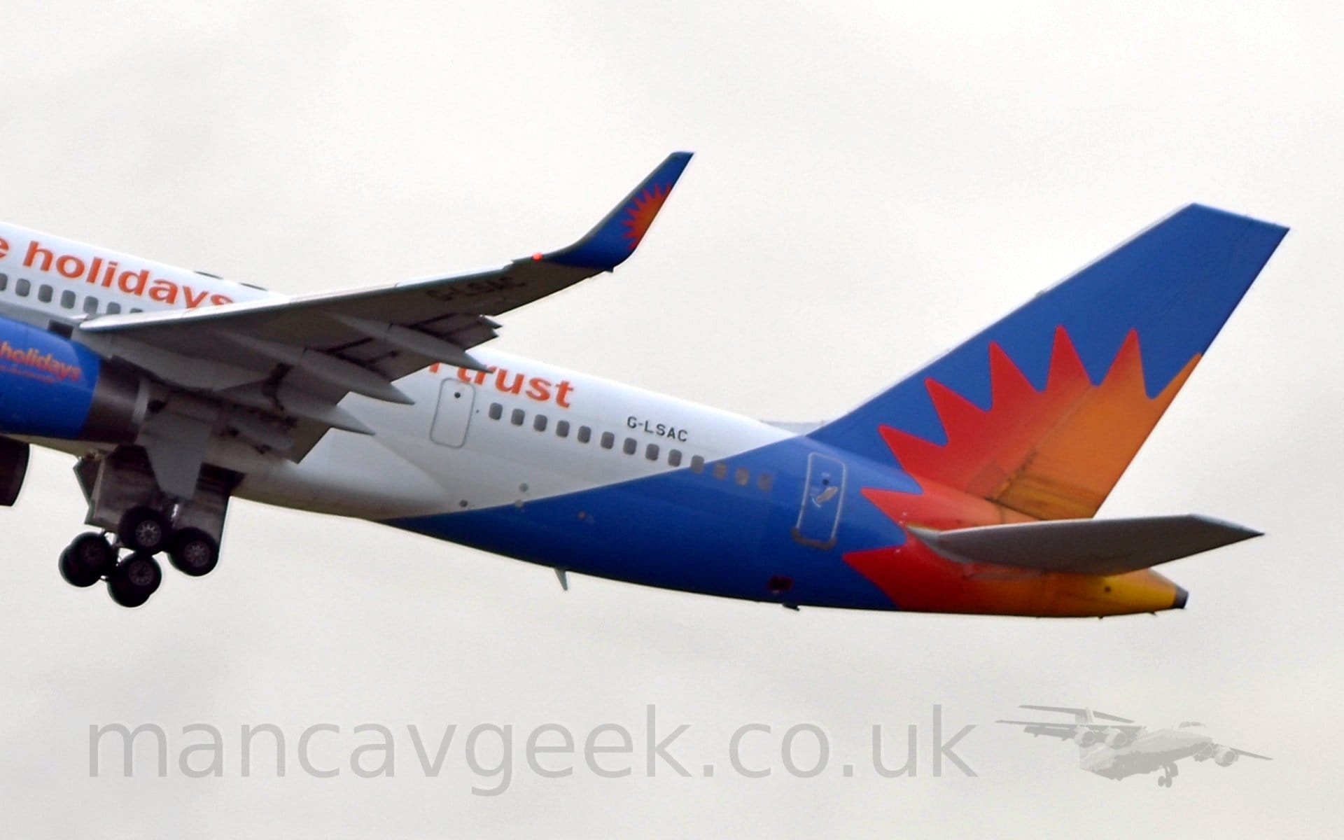 Closeup of the blue tail and rear fuselage of a white, twin engined jet airliner flying from left to right at a low altitude, with the undercarriage being retracted, flaps extended from the rear of the wings, and the nose raised significantly, suggesting it has just taken off.. There is a red, orange, and yellow sunburst at the lower rear of the tail, stretching over the rear fuselage. This same sunburst is repeated on the blue upturned wingtips. The blue engine pods are just visible on the left of the frame, with the word "holidays" printed on the side in a vertical yellow/orange/red gradient. There are words written on the side of the upper fuselage, but only "holidays" in front of the wing, and "trust" aft of the wing are discernible. The registration "G-LSAC" is visible in black on the upper rear fuselage, and under the left wing tip. In the background, thick white cloud fills the frame.