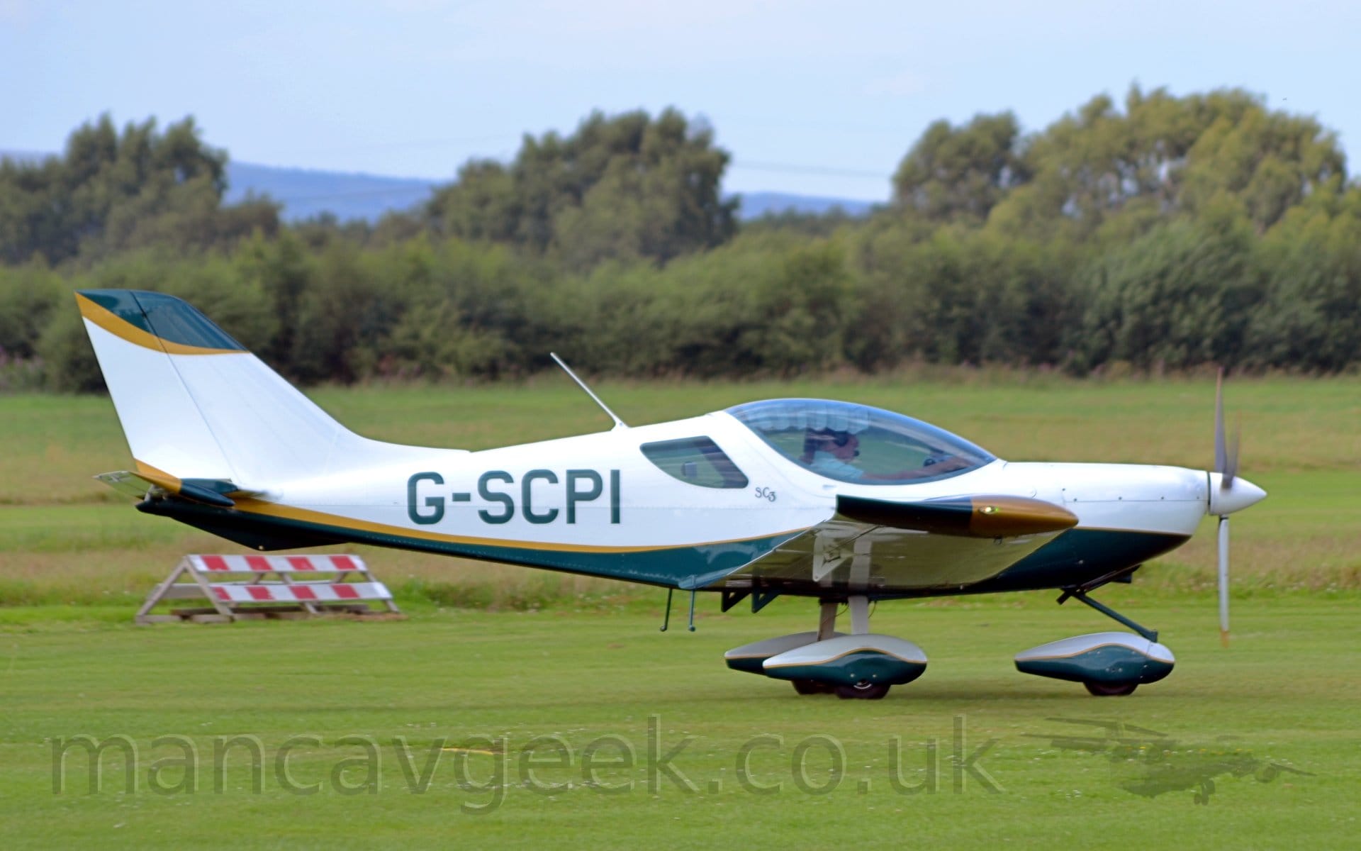 Side view of a white, single engined light aircraft taxiing from left to right on a grass airfield.  The plane is white on top, with a green belly.