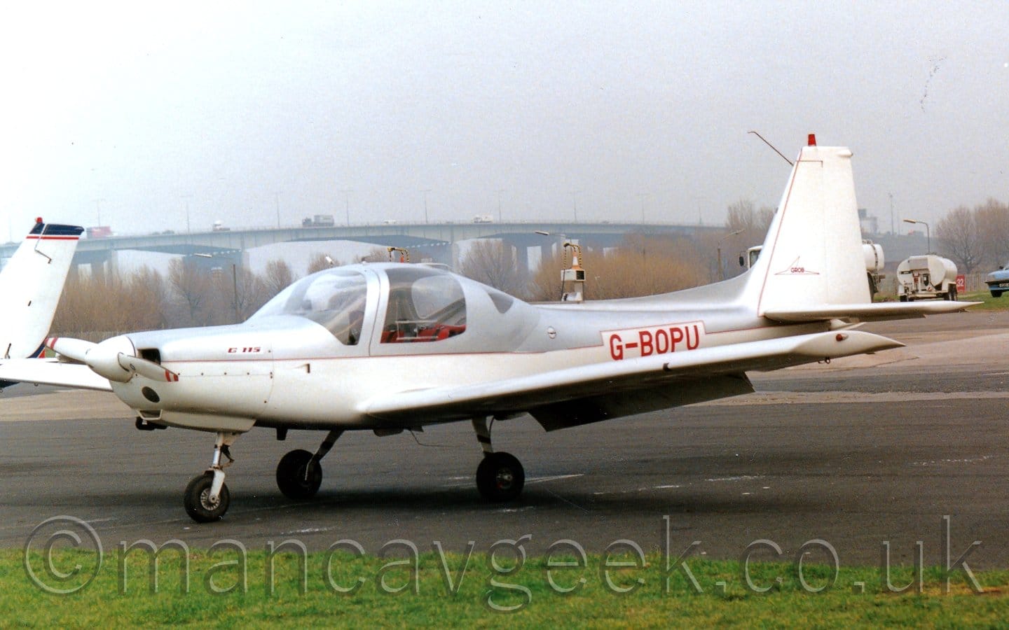 Side view of a white and grey, single engined light aircraft parked on tarmac facing to the left.