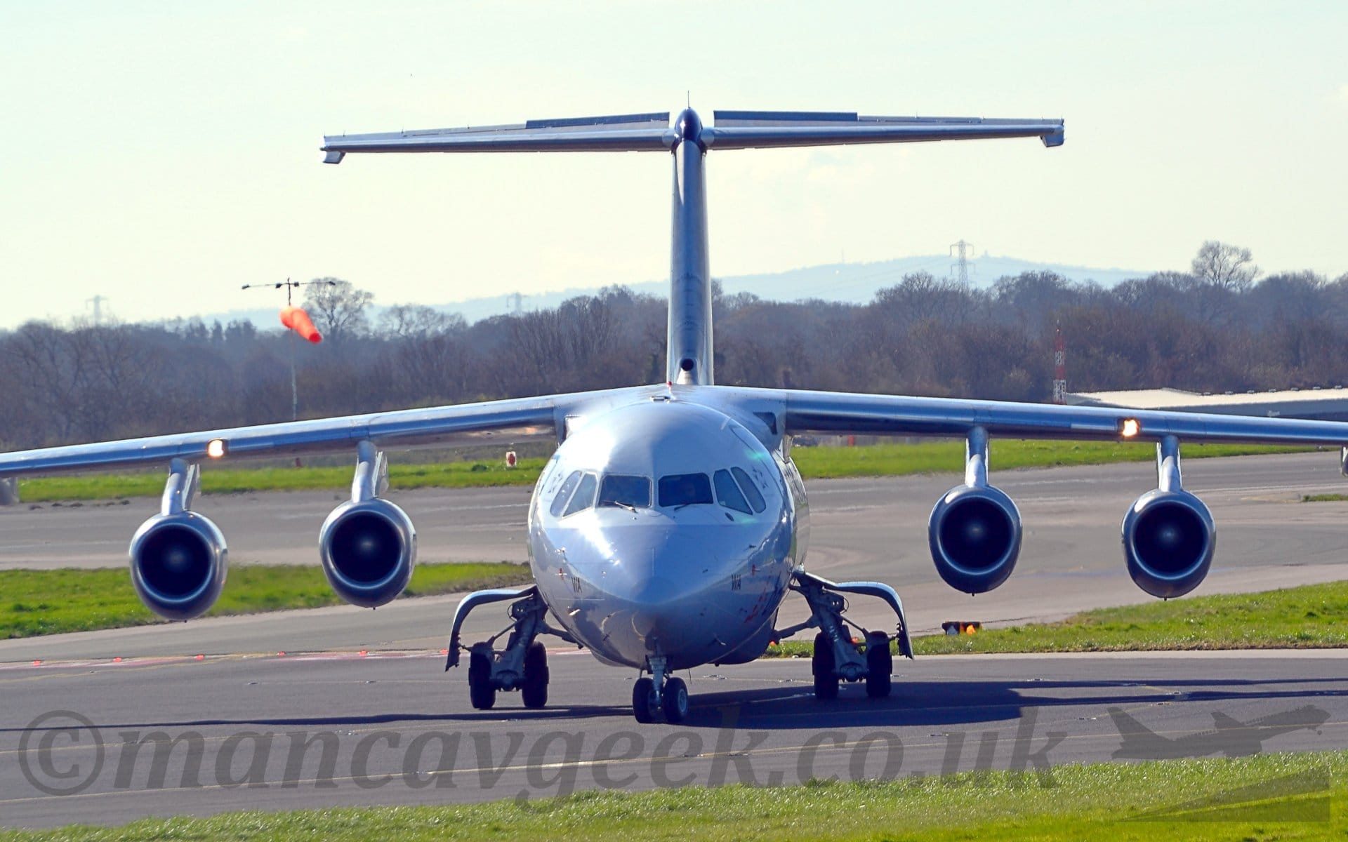 Head-on view of a high-winged, 4 engined jet airliner taxiing towards the camera, it's nose-wheel turned slightly to it's right.