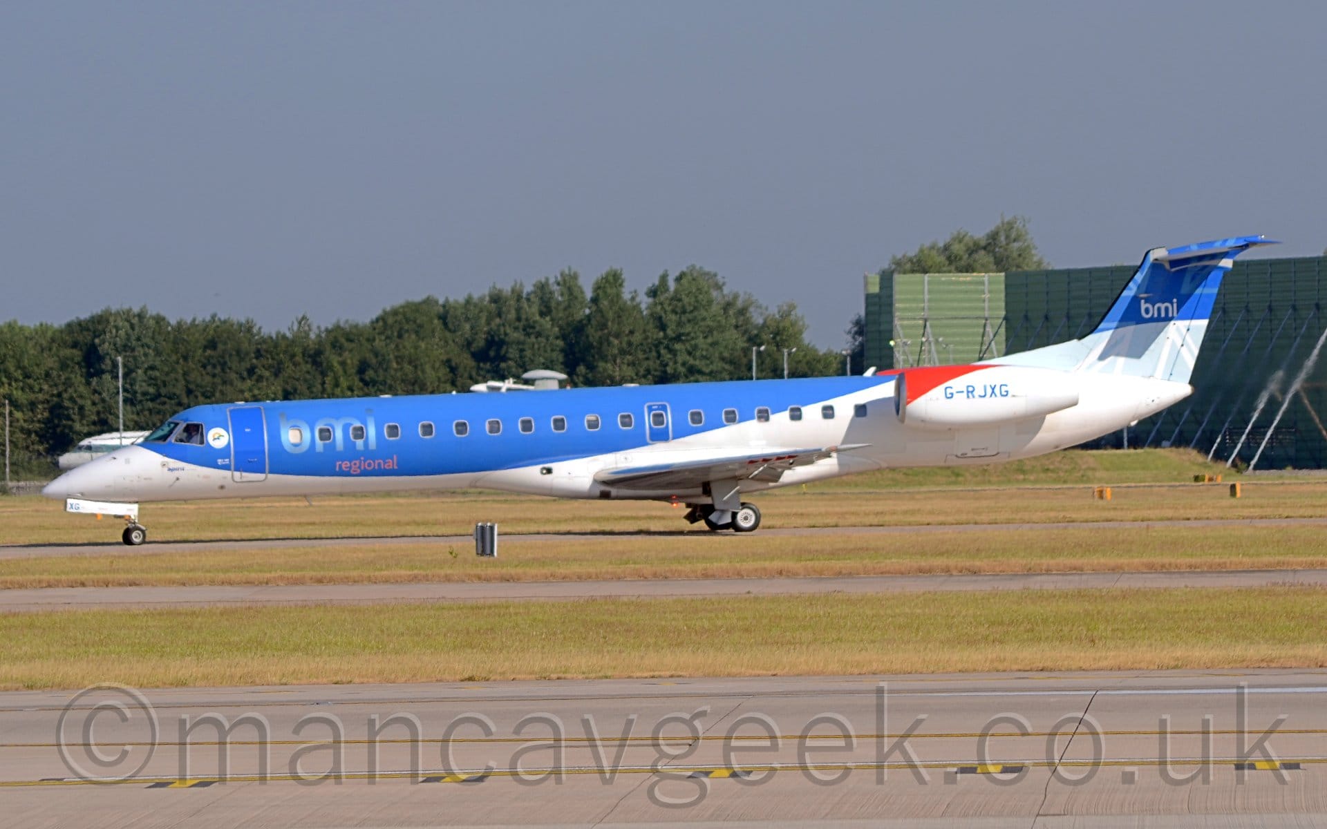 Side view of a twin engined jet airliner with the engines mounted on the sides of the rear fuselage, taxiing from right to left along a grey taxiway.