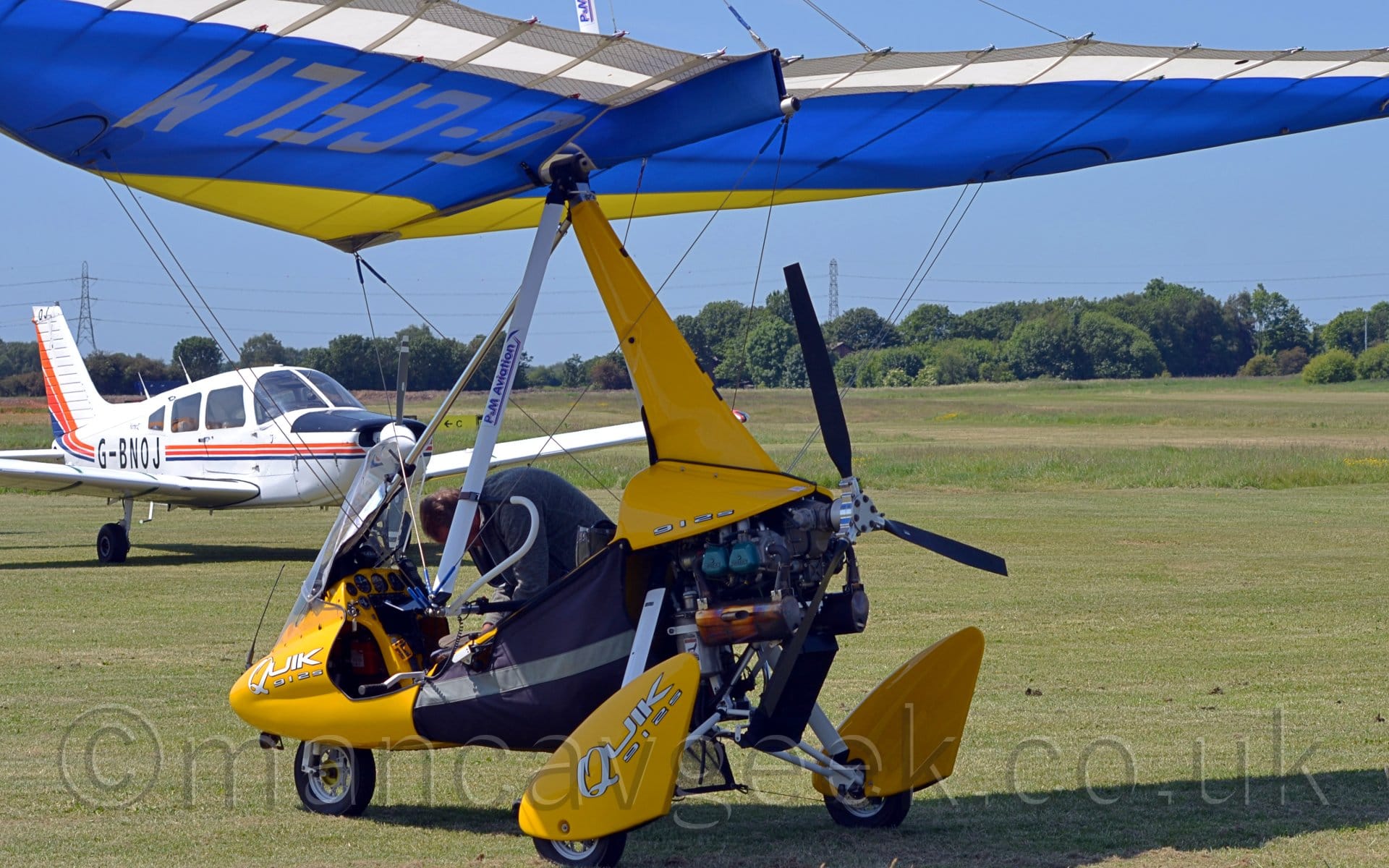 Rear side view of a single-engined microlight parked on grass facing to the left.