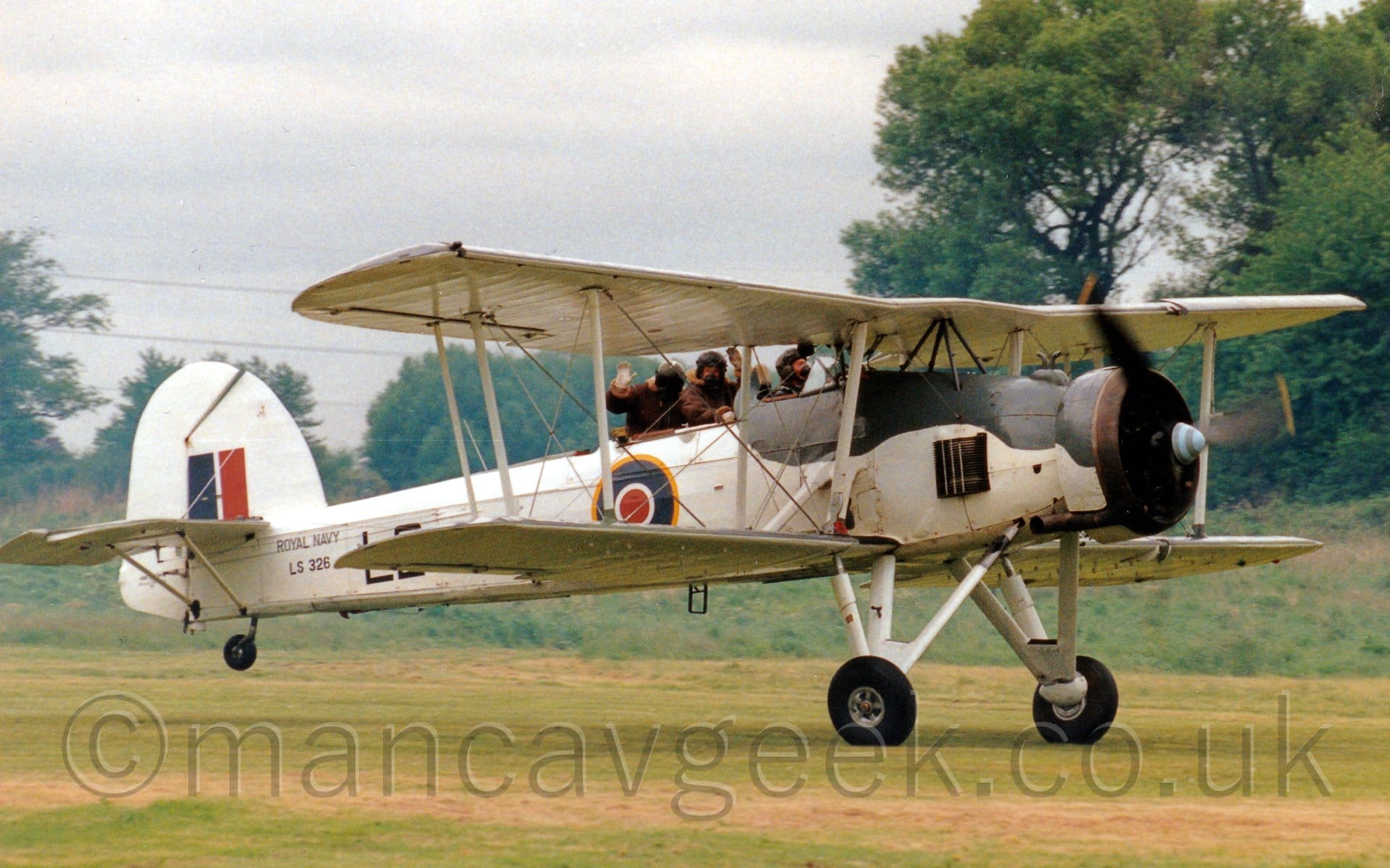 Side view of a large, single-engined bi-plane rolling along a grass runway with it's tail-wheel raised into a flying position.