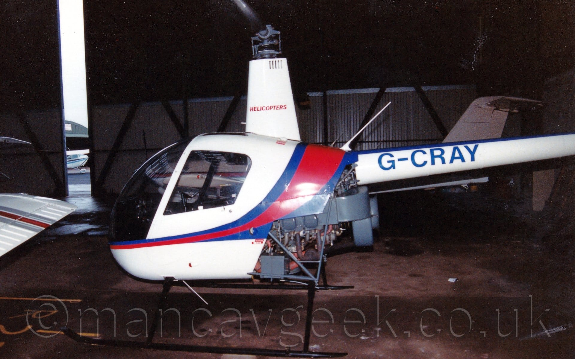 Side view of a small helicopter parked in a dark hangar, facing to the left.