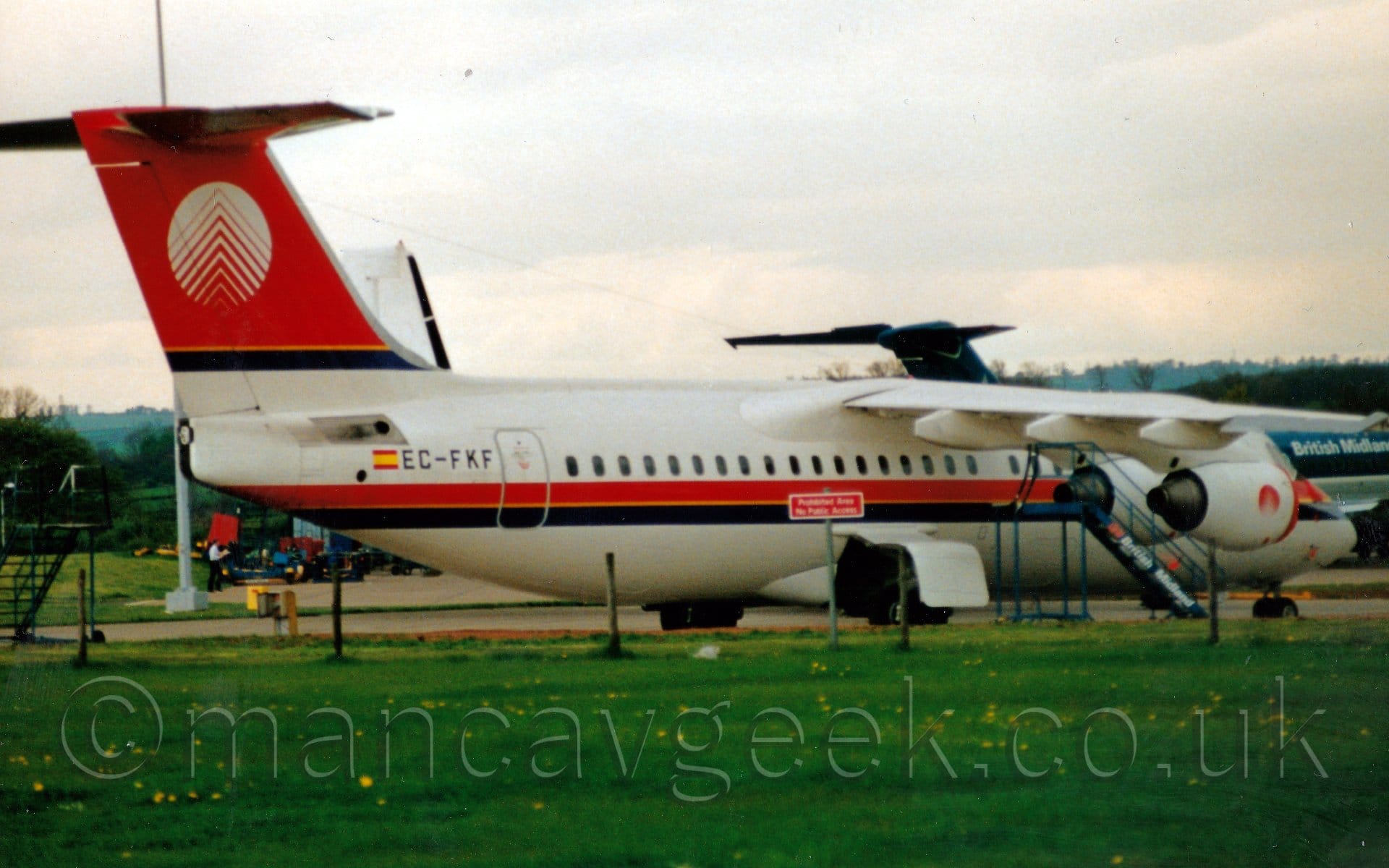 Side view of a white and red, high-winged, 4 engined jet airliner parked facing to the right.