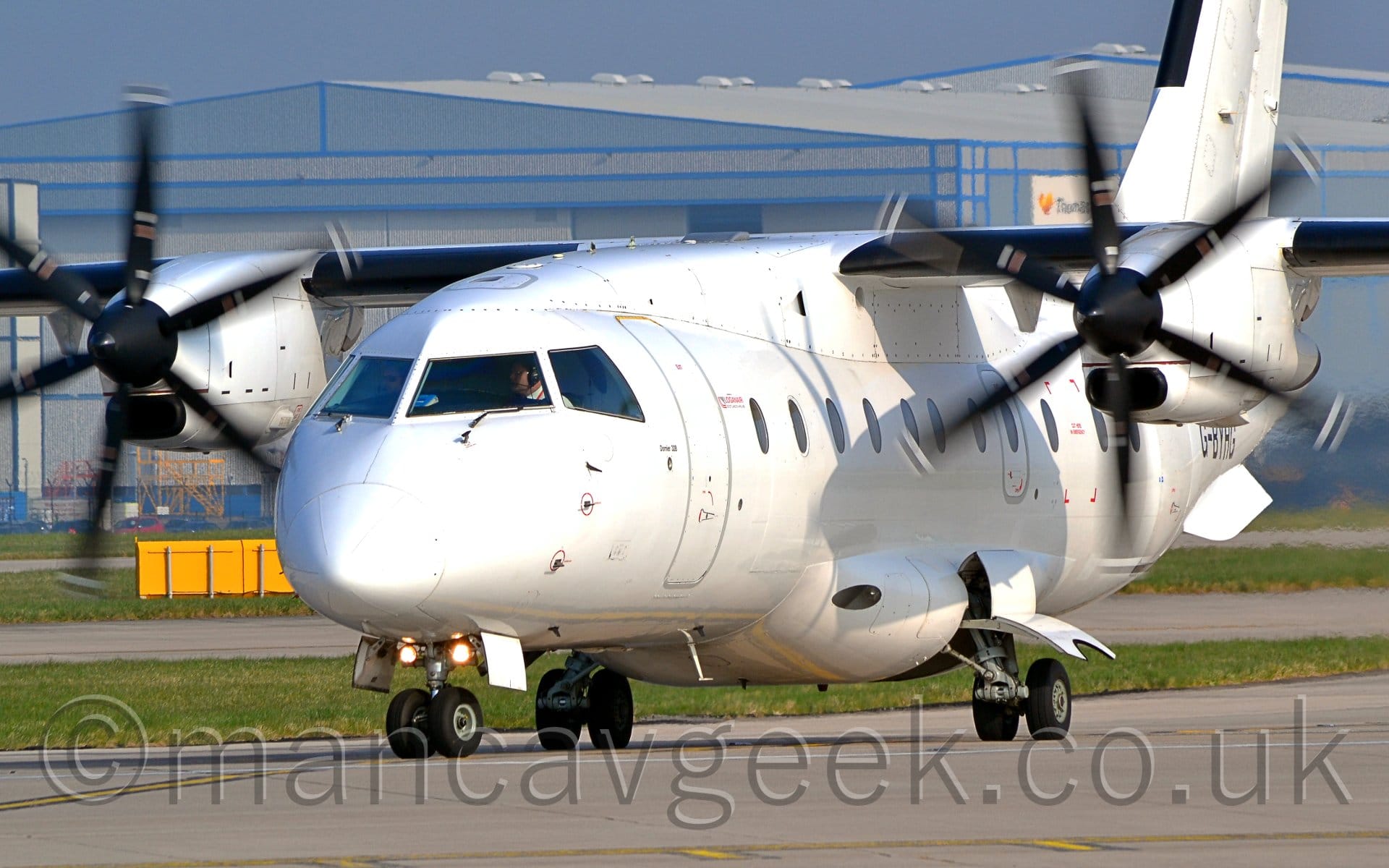 Side view of a white, high-winged, twin propellor-engined airliner taxiing from right to left.