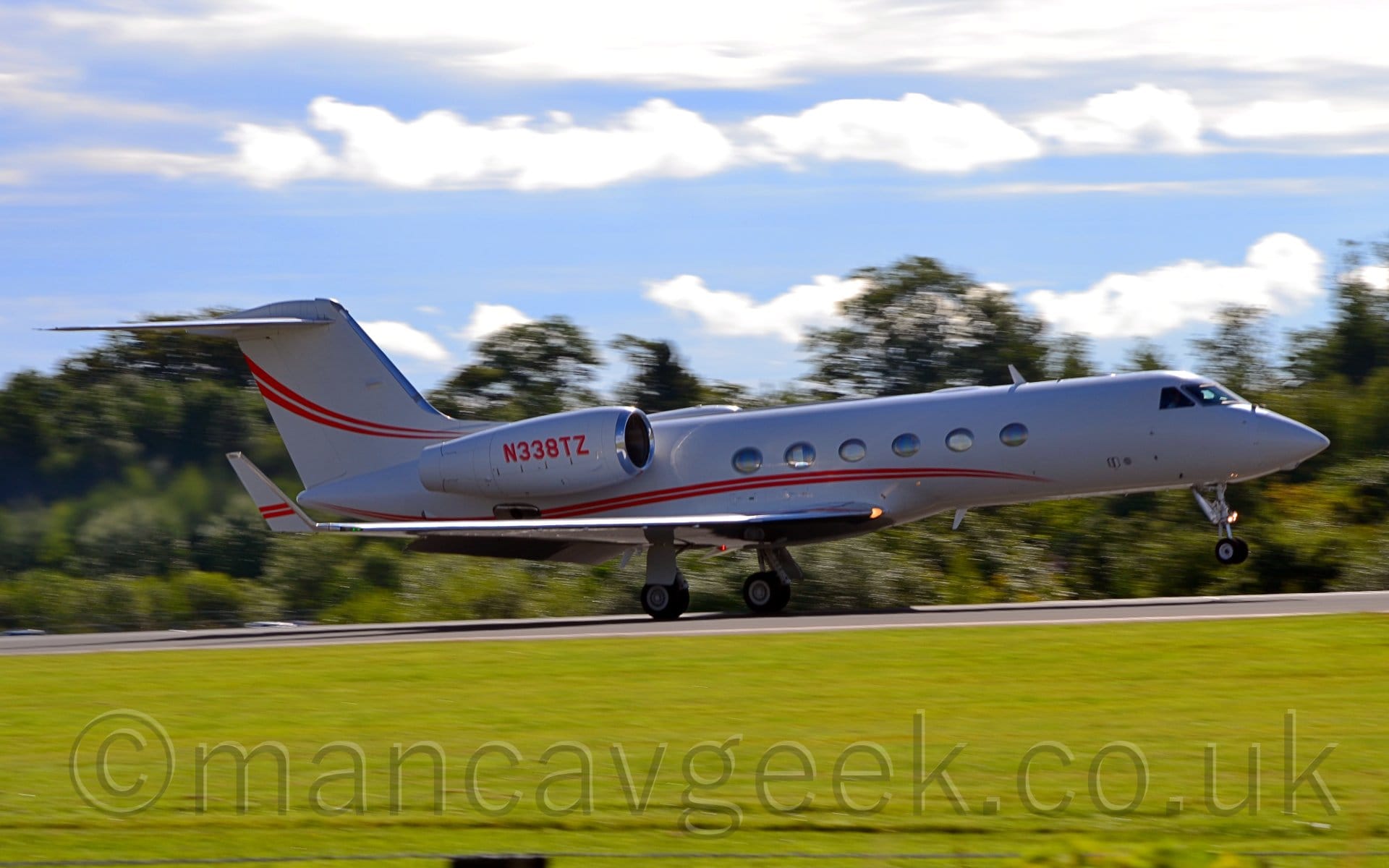 Side view of a white, twin engined BizJet moving at speed from left to right, flaps extended from behind the wings, and the nose raised, suggesting it is either taking off or landing.