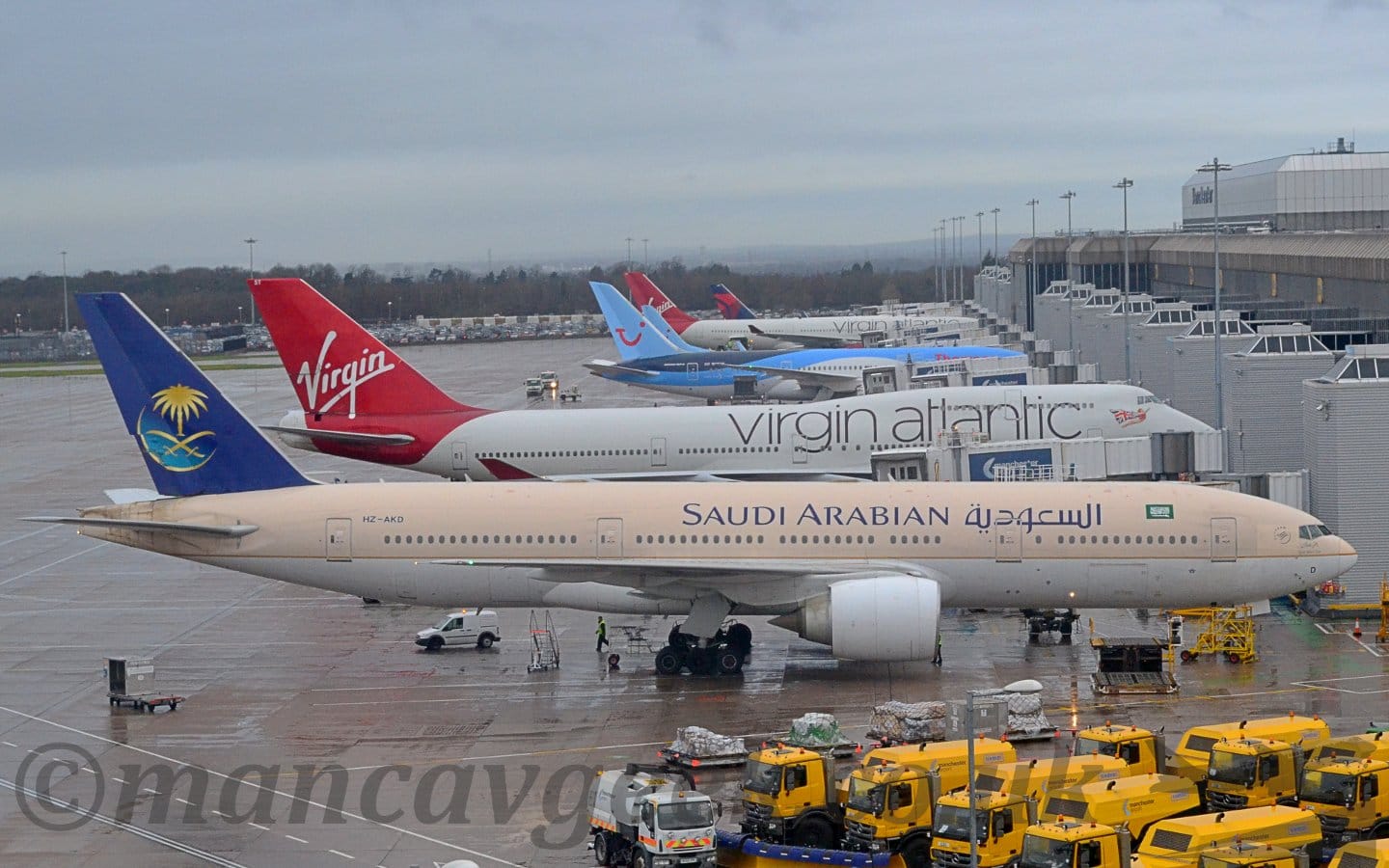 Side view of a twin engined jet airliner parked nose in to a grey terminal building.