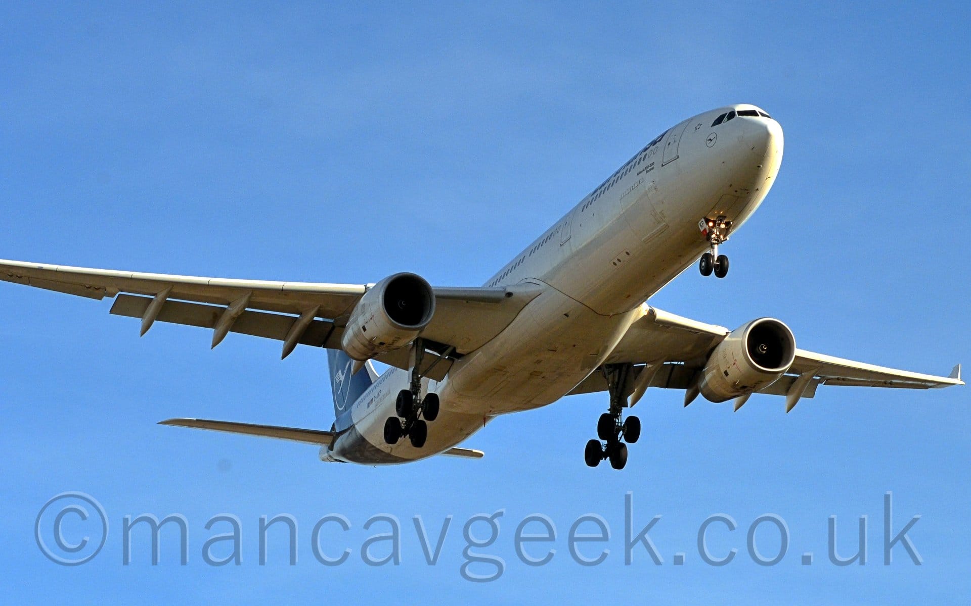 Low view of a white twin-engined jet airliner flying from left to right at a very low altitude