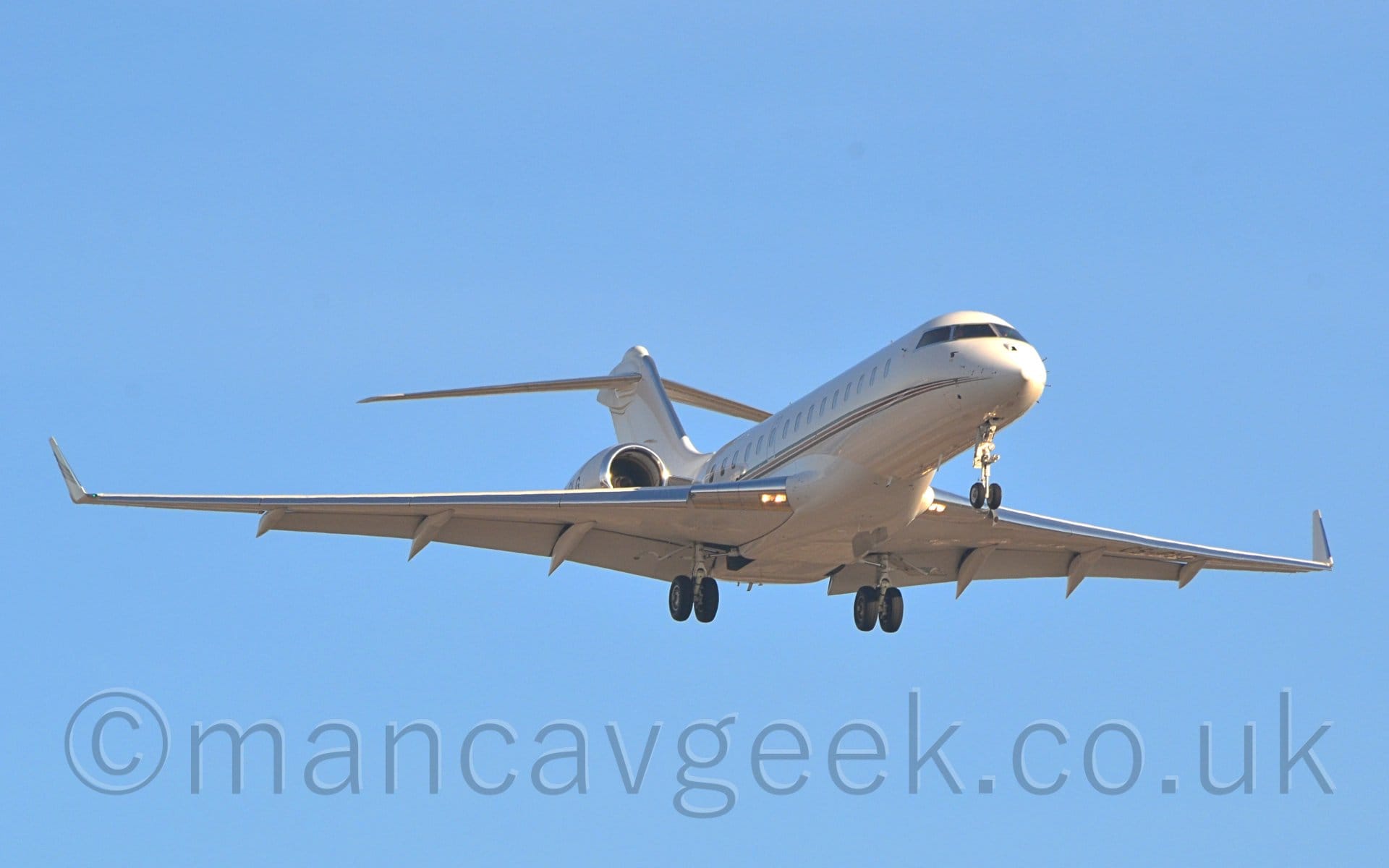 Low 3/4 view of a white, twin engined BizJet with the engines mounted on the sides of the rear fuselage, flying from left to right at a very low altitude