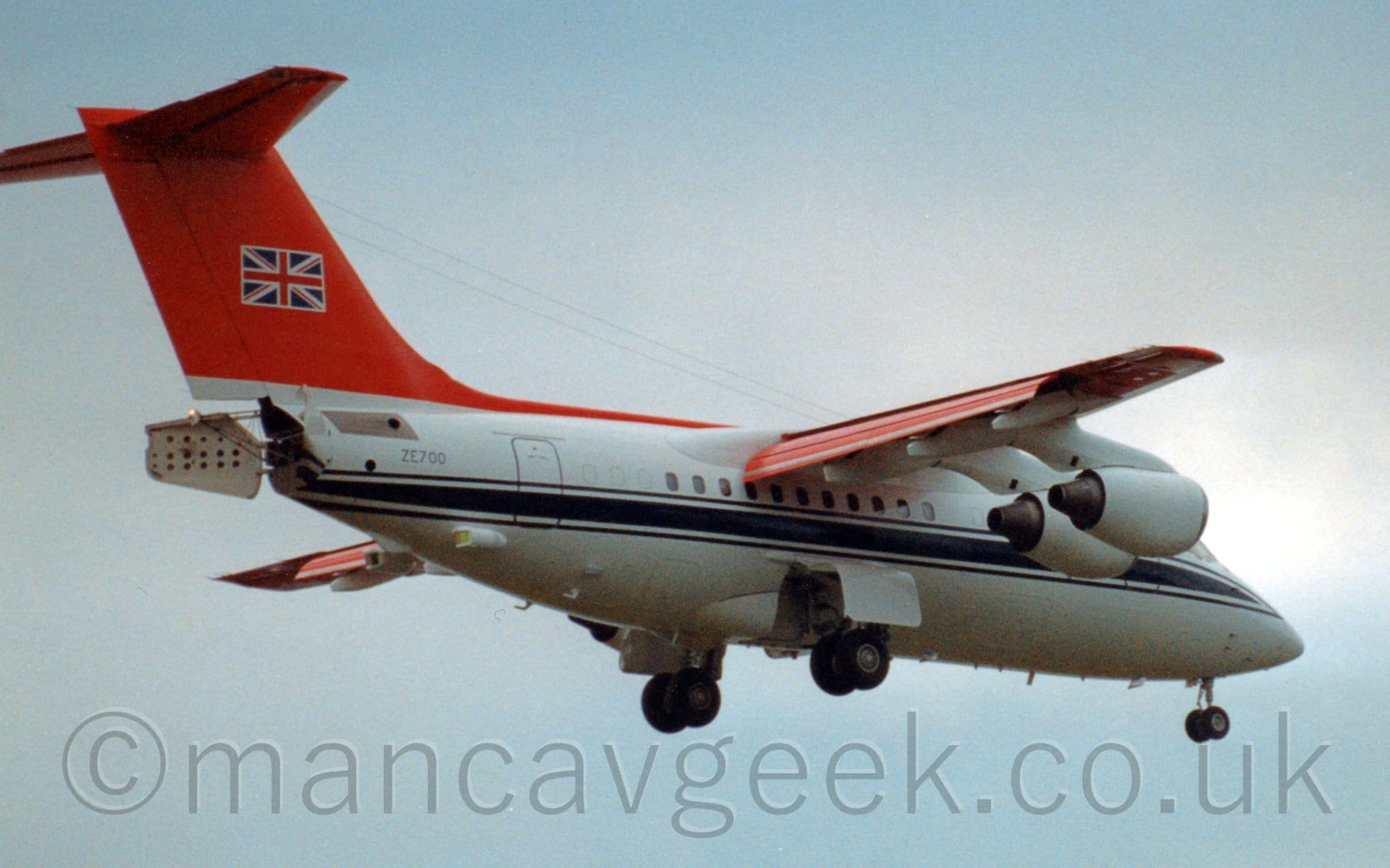 Side view of a high-winged, 4 engined jet airliner flying from left to right at a very low altitude.