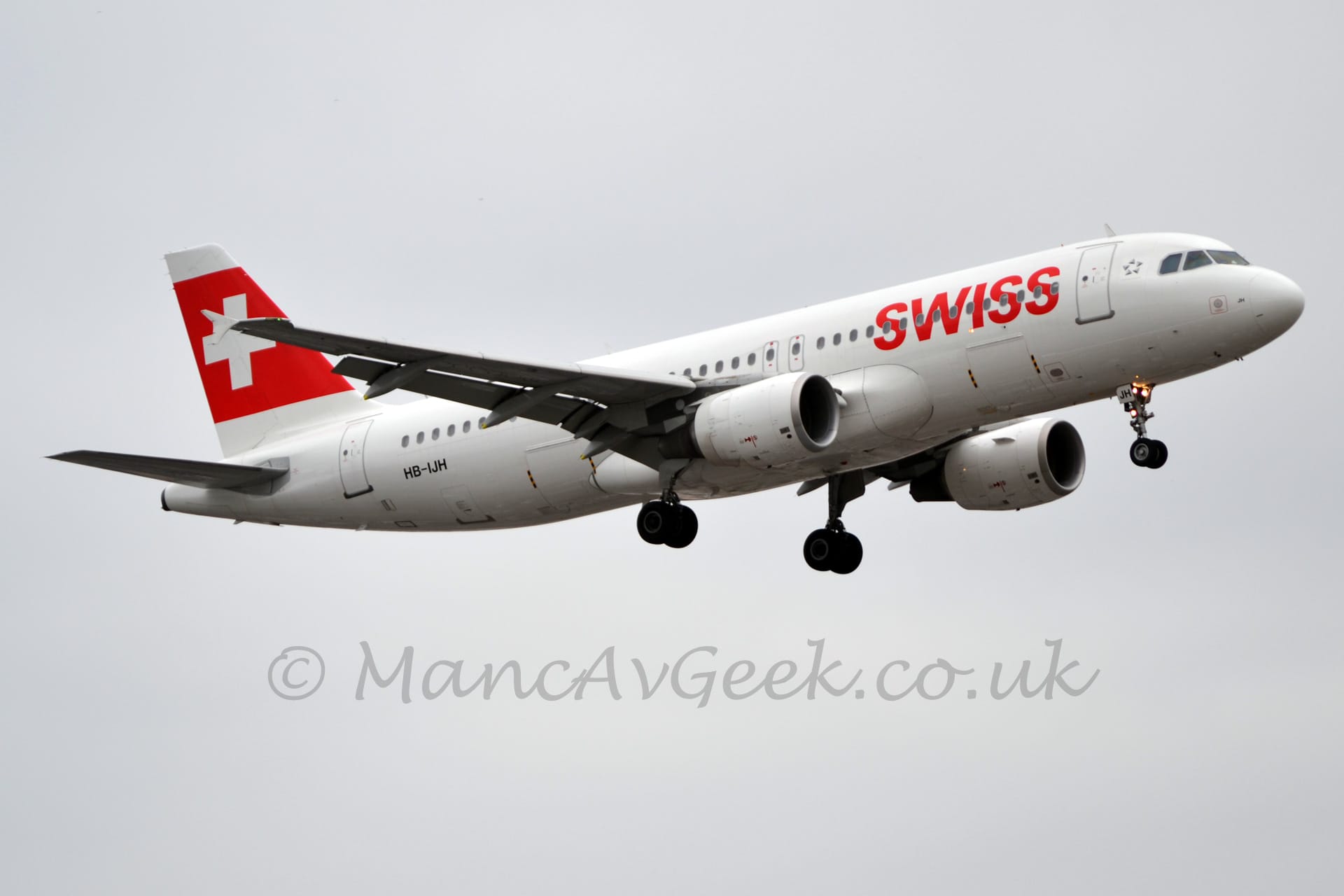 Side view of a white, twin engined jet airliner flying from left to right at a low altitude.