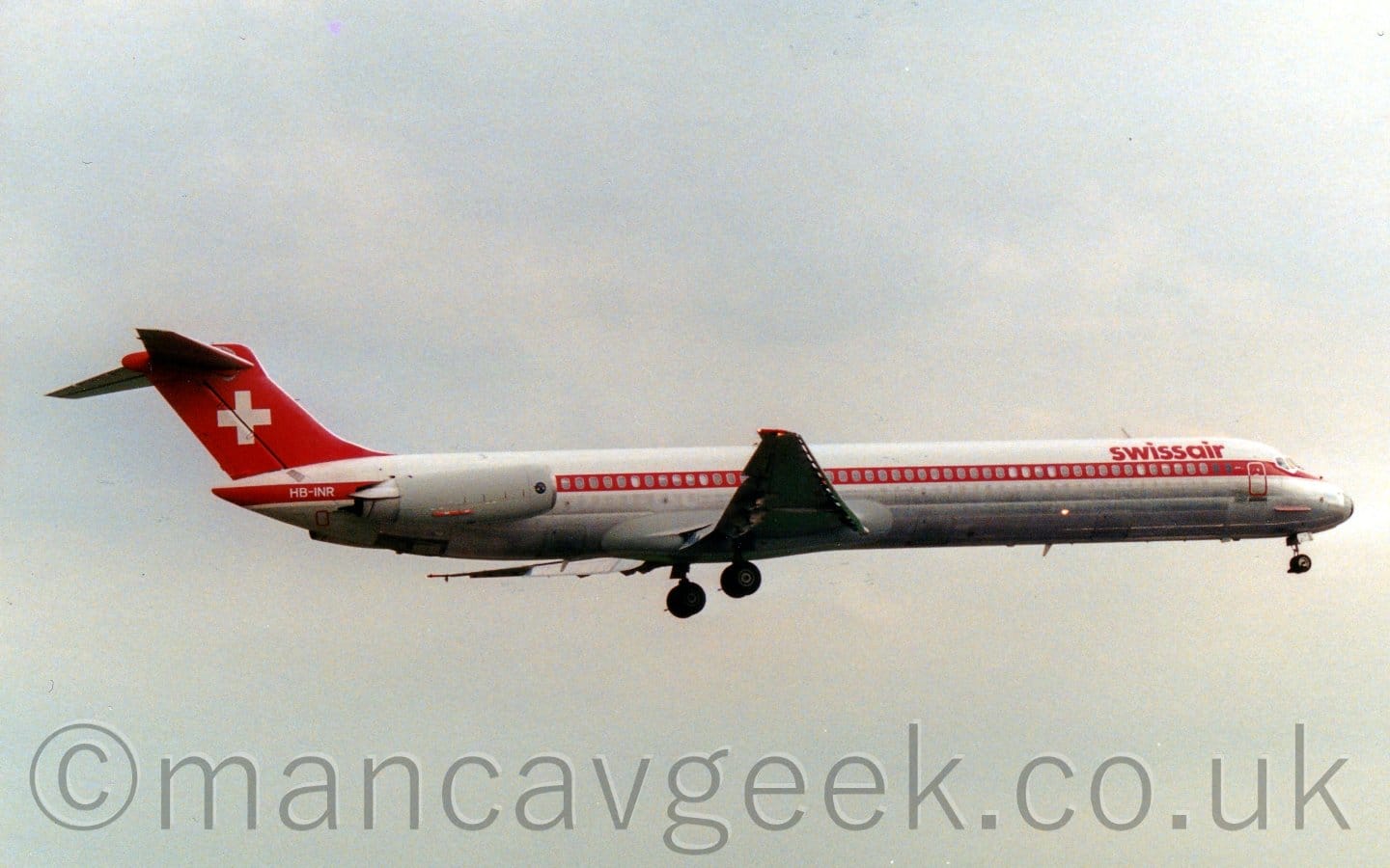 Side view of a twin engined jet airliner with the engines mounted on the sides of the rear fuselage, flying from left to right at a low altitude