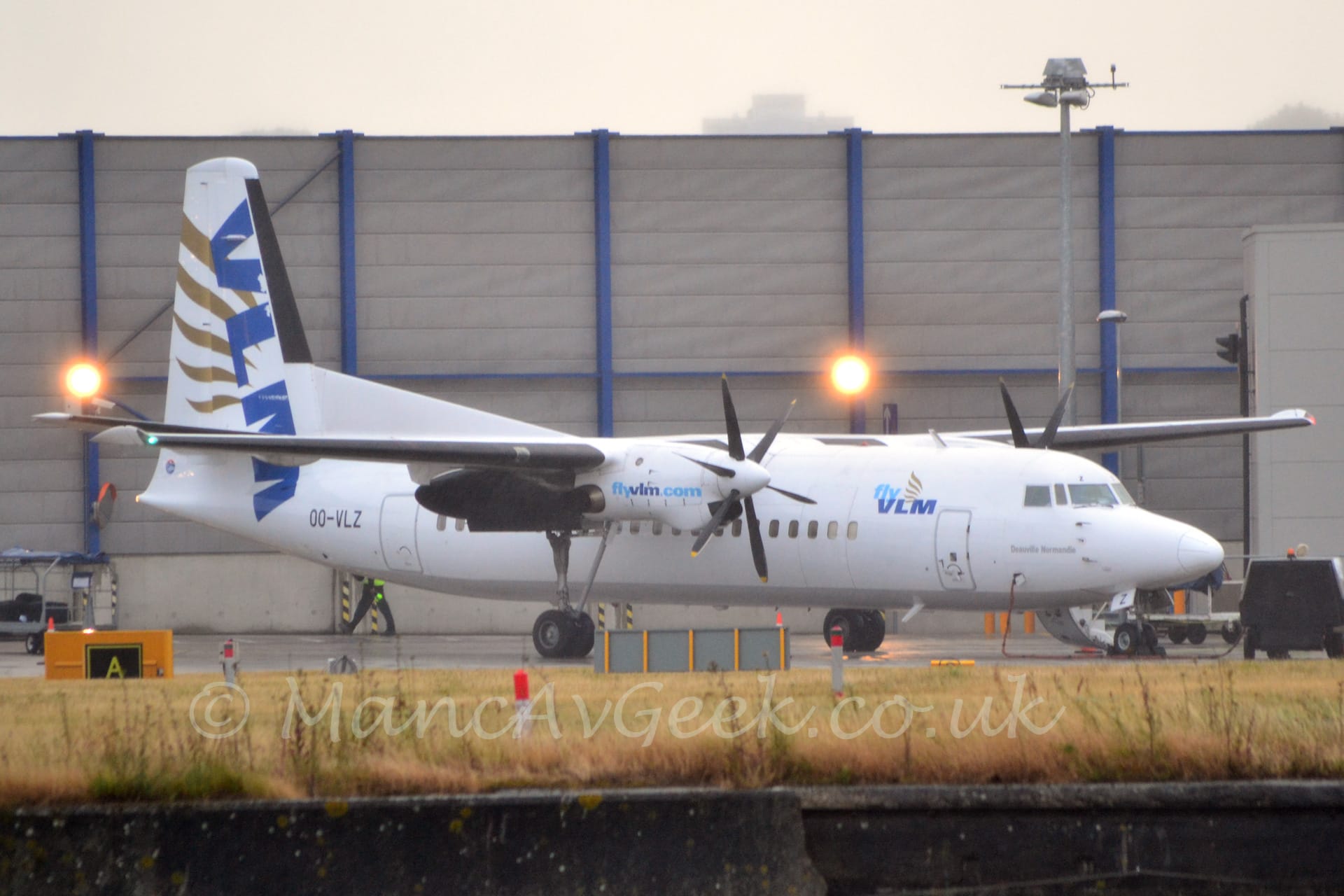 Side view of a high-winged, twin propellor-engined airliner parked facing to the right.
