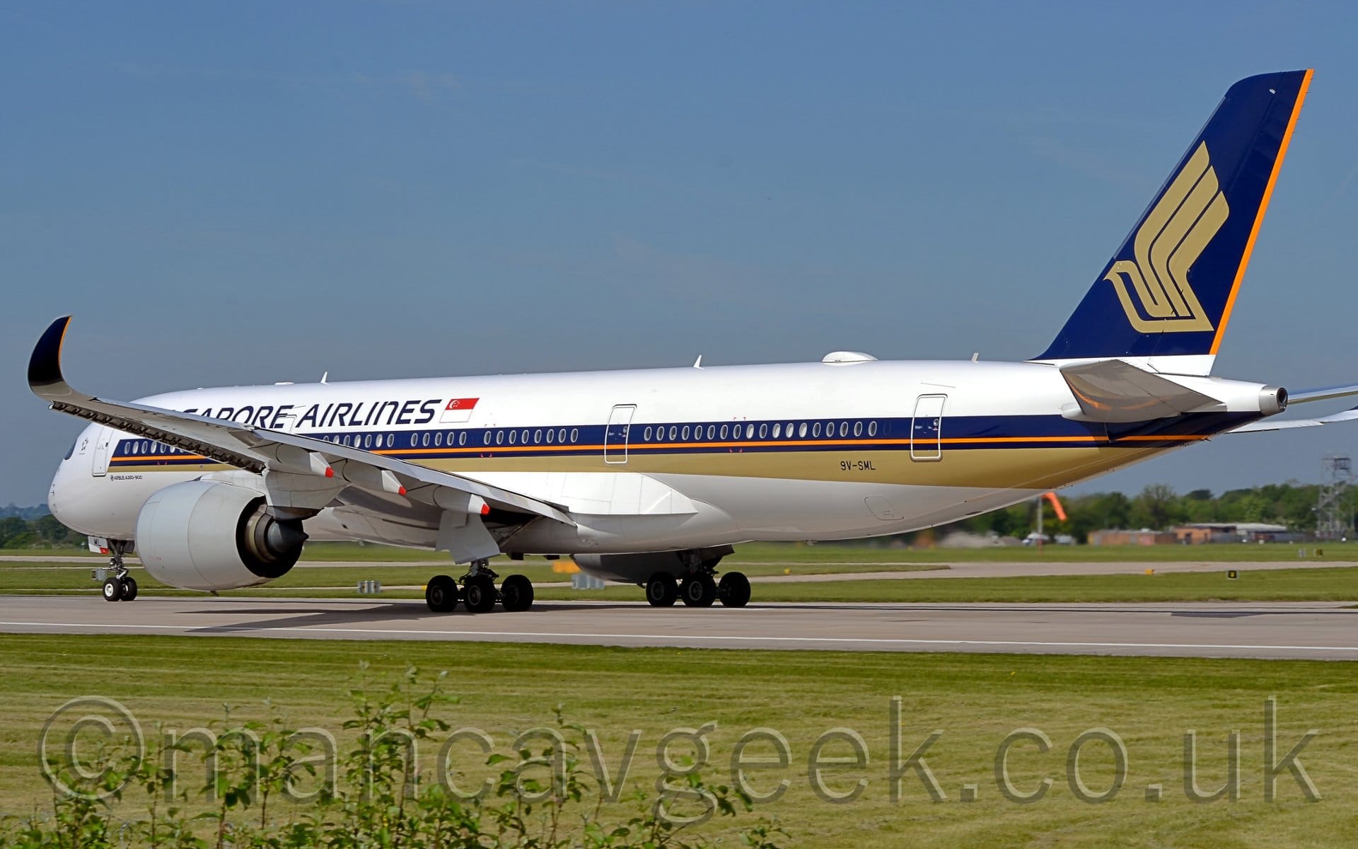 Rear side view of a twin engined jet airliner moving from right to left along a dark grey runway.