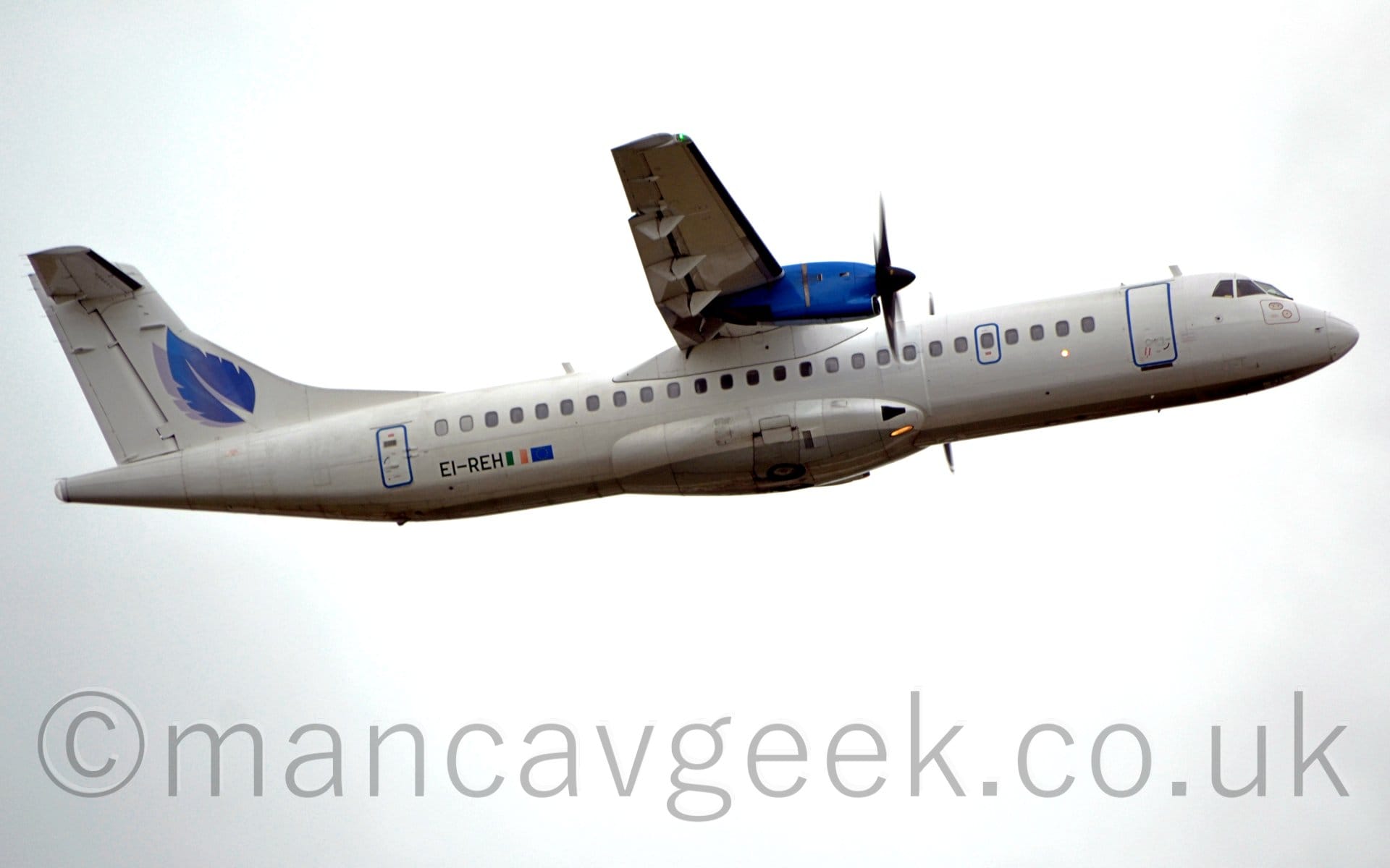 Side view of a white, high-winged, twin propellor-engined airliner flying from left to right at a very low altitude