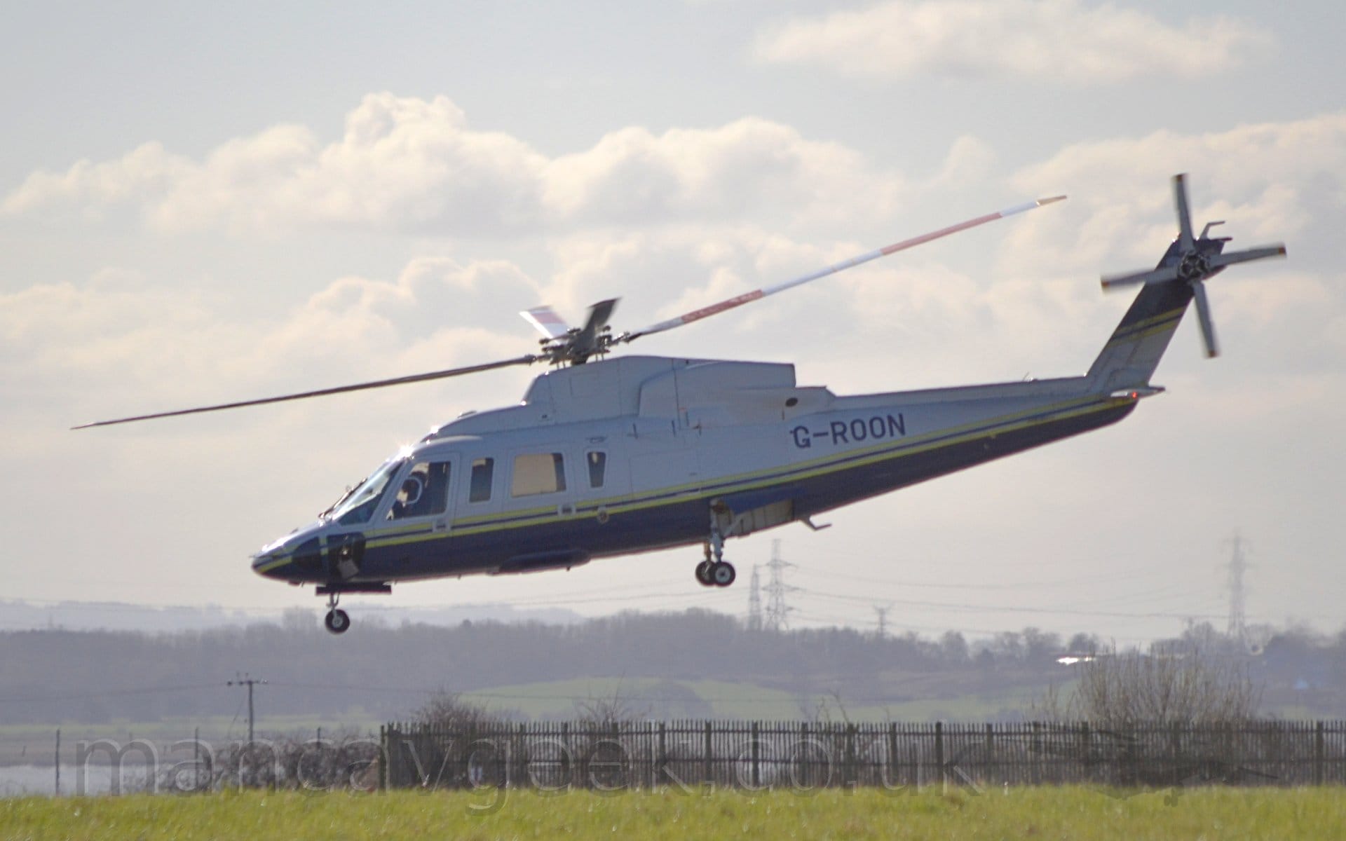 Side view of a helicopter flying from right to left at a low altitude with it's undercarriage extended.