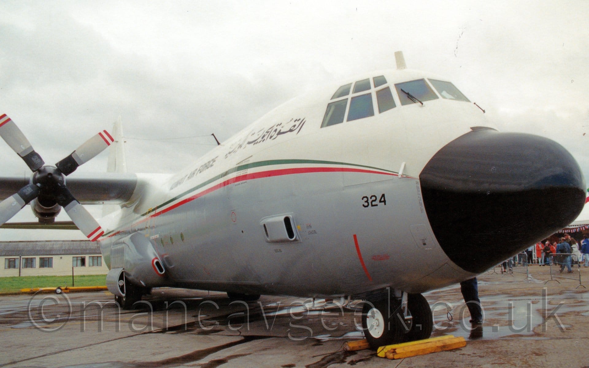 Front side view of the nose and forward fuselage of a high-winged, 4 propellor-engined military cargo plane parked facing to the right.