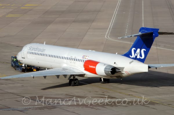 Rear side view of a white, twin engined jet airliner with the engines mounted on the rear fuselage, facing to the left