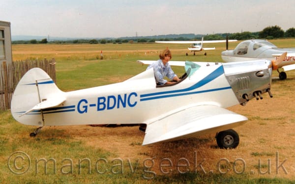 Side view of a white, single seat, single engined light aircraft parked on grass facing to the right.