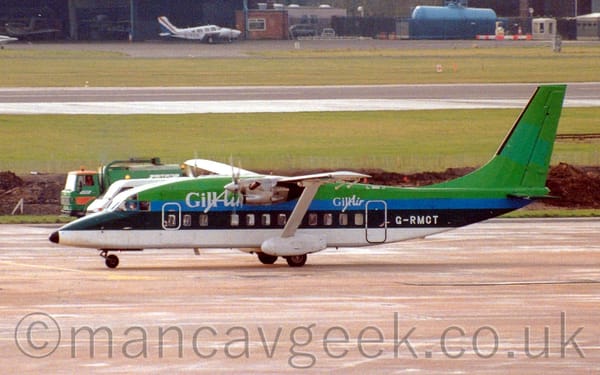 Side view of a green, blue, and white, high-winged, twin propellor-engined airliner taxiing from right to left.