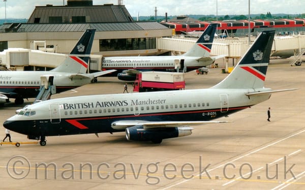 Side view of a grey, twin engined jet airliner with a dark blue (almost black) lower half, facing to the left