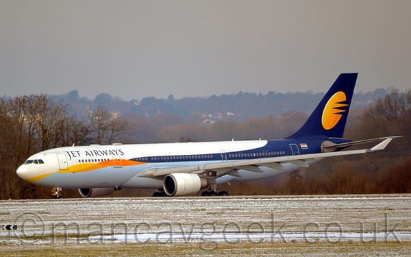Side view of a white, twin engined jet airliner with a grey belly taxiing from right to left.