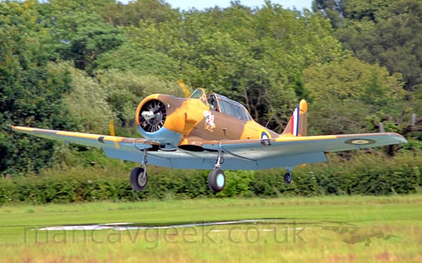 Side view of a World War 2-era, single propellor-engined military trainer aircraft flying from right to left at a very low altitude