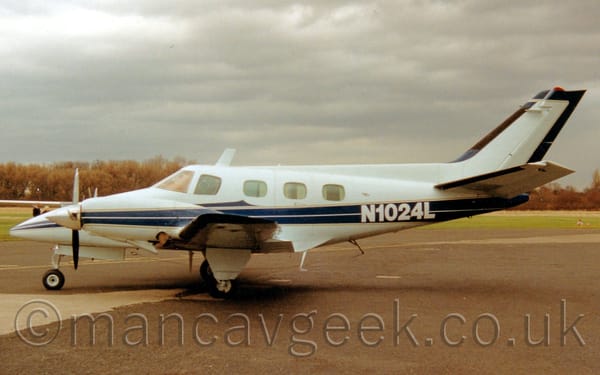 Side view of a twin propellor-engined BizProp parked on concrete facing to the left.