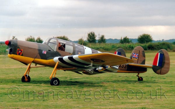 Side view of a small, single propellor-engined light aircraft with 3 tail-fins, and olive green and brown camouflage 