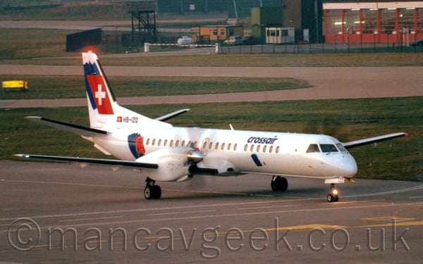 Side view of a white, twin propellor-engined airliner taxiing from left to right.