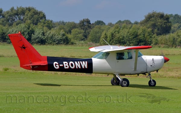 Side view of a high-winged, single-engined light aircraft taxiing from left to right on grass.