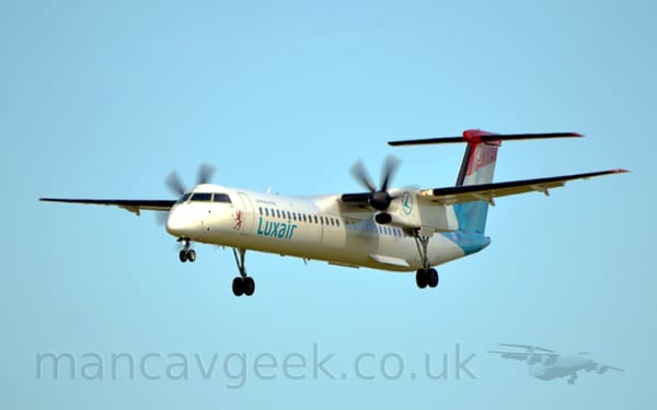 Side view of a white, high-winged, twin propellor-engined plane flying from right to left at a low altitude