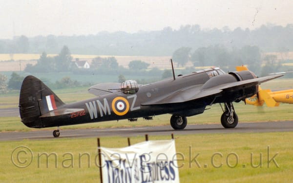 Side view of a twin propellor-engined military bomber aircraft taxiing  along a black runway from left to right.
