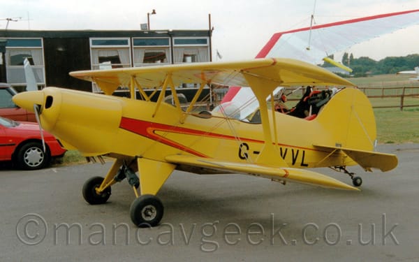 Side view of a yellow, single-engined bi-plane parked facing to the left.
