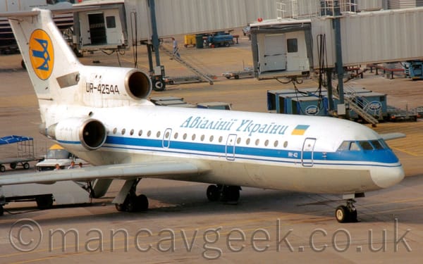 Side view of a white, 3 engined jet airliner with the engines mounted on the rear fuselage, parked facing to the right.