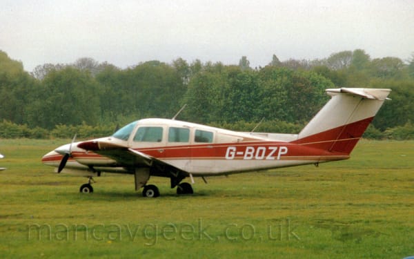 Side view of a cream-coloured, twin engined light aircraft parked on grass facing to the left.