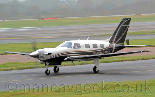 Side view of a white and black, single-engined Bizprop taxiing from right to left along a black taxiway.
