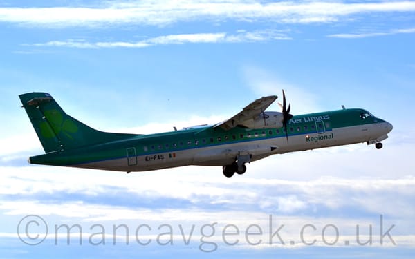 Side view of a green, high-winged, twin propellor-engined airliner flying from left to right at a low altitude