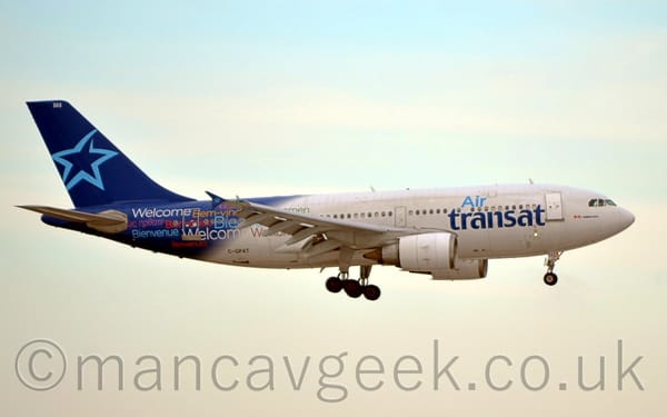 Side view of a white and blue, twin engined jet airliner flying from left to right at a very low altitude, with undercarriage extended, suggesting it is about to land.