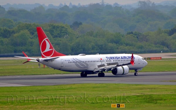 Side view of a twin engined jet airliner moving from left to right on a black runway.