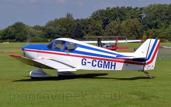 Side view of a white, single-engined light aircraft taxiing from right to left on a grass airfield.