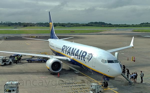 Side view of a white and blue, twin engined jet airliner parked facing to the right.