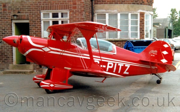Side view of a small, red, single-engined bi-plane light aircraft parked facing to the left.