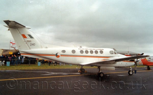 Side view of a white, twin engined Bizprop parked on a black tarmac taxiway facing to the right.