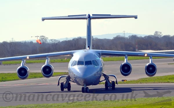 Head-on view of a high-winged, 4 engined jet airliner taxiing towards the camera, it's nose-wheel turned slightly to it's right.