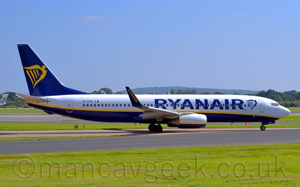 Side view of a twin engined jet airliner taxiing from left to right along a grey taxiway.