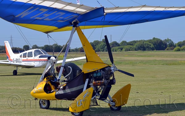 Rear side view of a single-engined microlight parked on grass facing to the left.