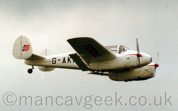 Side view of a twin engined light aircraft flying from left to right at a low altitude, with flaps extended from behind the wings.