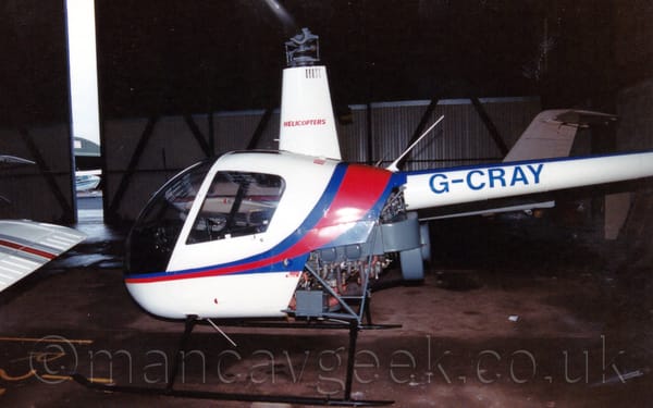 Side view of a small helicopter parked in a dark hangar, facing to the left.